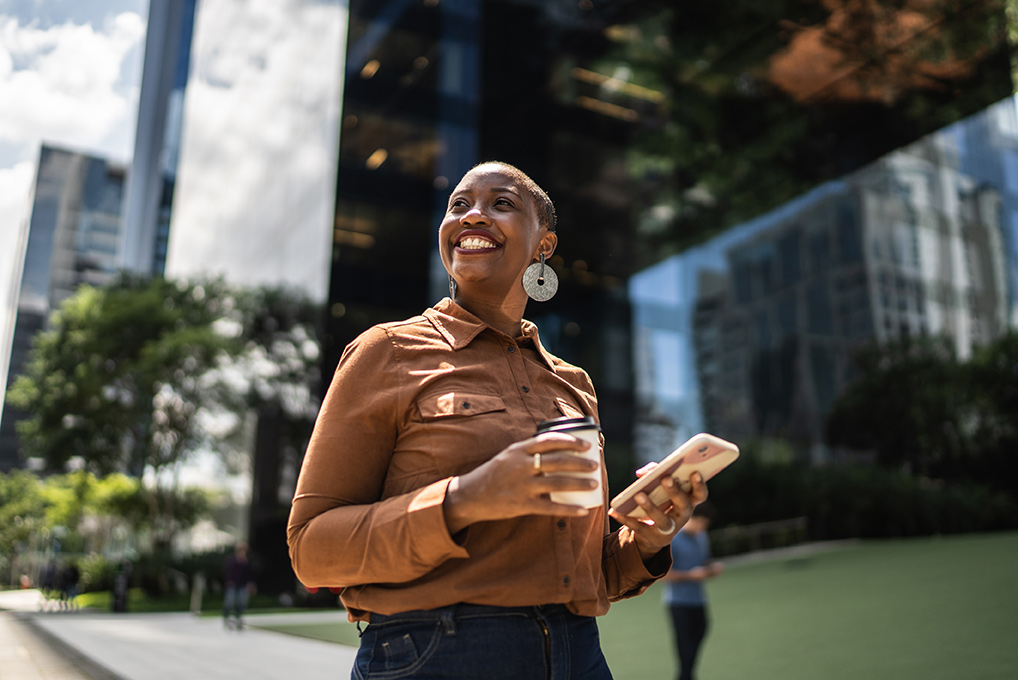 Femme souriante marche avec un café et son téléphone à la main
